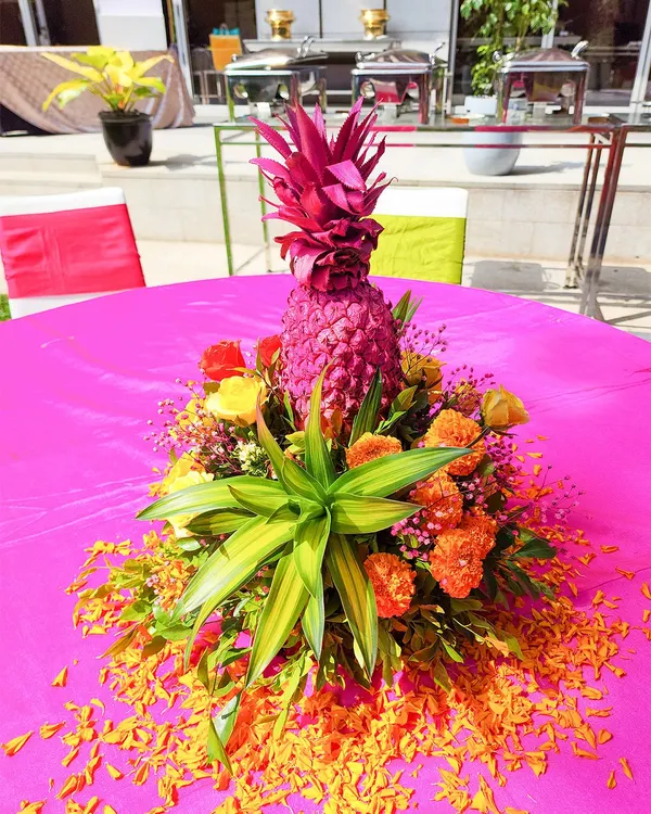 A unique and vibrant centerpiece perfect for a Haldi or tropical-themed event. We used a painted pink pineapple surrounded by bright orange marigolds and lush green leaves to create a fun and festive table decoration.