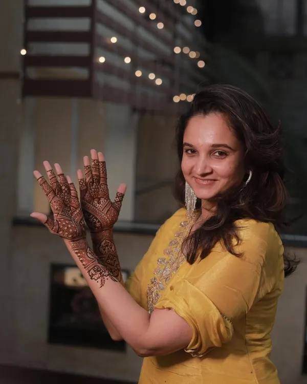 A happy guest showing off her party mehendi against a backdrop of festive lights.