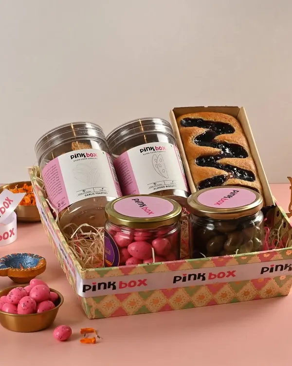This is our "Gulal" hamper, a vibrant mix of sweet and savory treats. It includes Almond Biscotti, Garlic Toasties, a Blueberry Marble Cake, Pink Almond Dragees, and Chocolate Coated Cashews.
