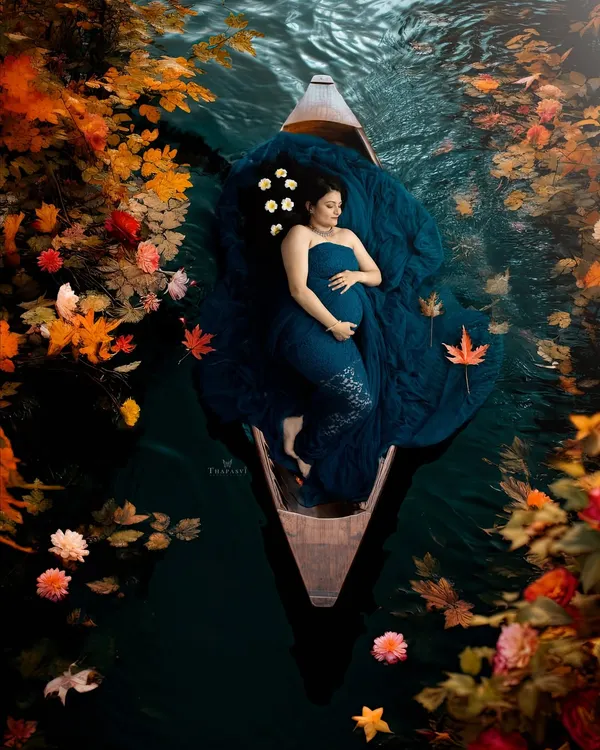 A breathtaking and artistic overhead shot. The mother-to-be floats peacefully in a boat, surrounded by autumn leaves, creating a stunning, painterly image of serenity.
