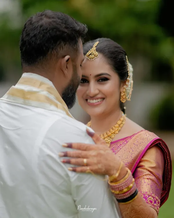 A beautiful over-the-shoulder shot where the bride looks directly at the camera with a radiant smile. This captures a perfect, heartfelt connection in a lush garden setting.