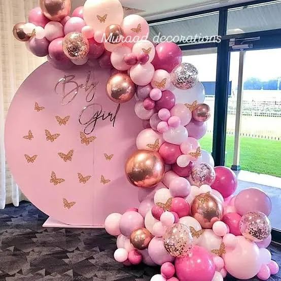 A beautiful 'Baby Girl' announcement setup for a baby shower. The design features a pink circular backdrop with butterfly decals, framed by a stunning balloon garland in shades of pink, rose gold, and confetti.