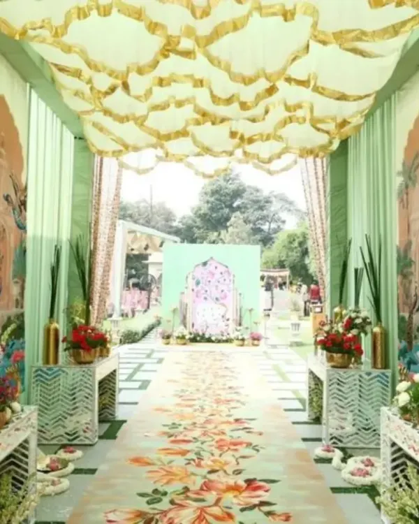 An elaborate entrance for a Pichwai-themed Mehendi. This setup features a custom-printed floral walkway, pastel green drapes with traditional motifs, and an ornate ceiling treatment, leading to the main event area.