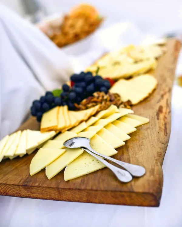 Our cheese boards are a celebration of European indulgence. This rustic wooden platter features a curated selection of fine cheeses, accompanied by fresh grapes and walnuts for a perfect pairing.