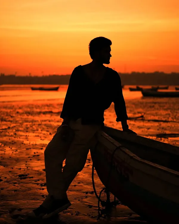 A classic silhouette shot against a fiery orange sunset on the beach. This dramatic lighting is perfect for creating moody and artistic portraits for a male model's portfolio.
