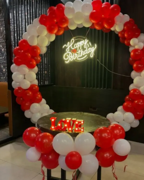 A simple and classic red and white balloon ring, perfect for smaller spaces or as an addition to a larger decor scheme. The setup includes a neon sign and a "LOVE" marquee, ideal for an intimate anniversary or Valentine's celebration.