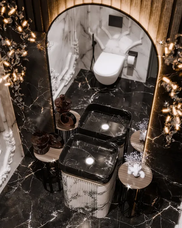 A top-down view of a dramatic powder room, showcasing the contrast between the black marble floor and the monolithic white marble pedestal sink. The render captures the glow of the sculptural lights.