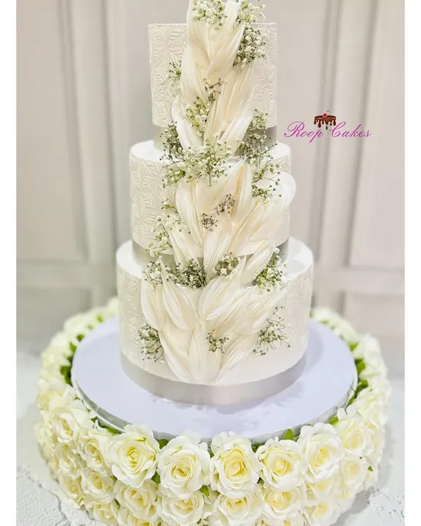 This grand three-tier wedding cake is pure elegance. The design features delicate wafer paper feathers cascading down the sides, accented with sprays of baby's breath for a look that is both modern and timeless.