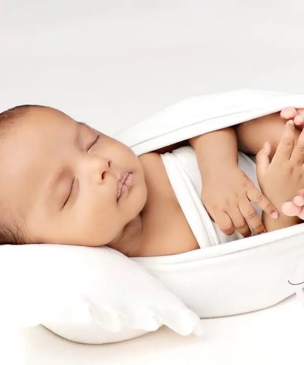 A newborn rests in a 'potato sack' pose in a pure white setup. This minimalist approach creates a timeless, angelic portrait.