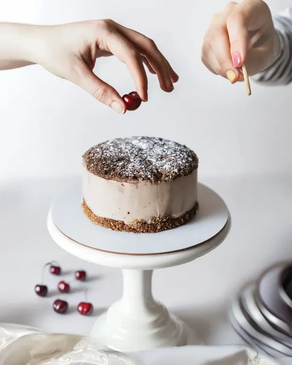 A behind-the-scenes look at the art of food styling, with hands carefully placing a cherry on a chocolate cake. This type of shot tells a story of craftsmanship and fresh ingredients.