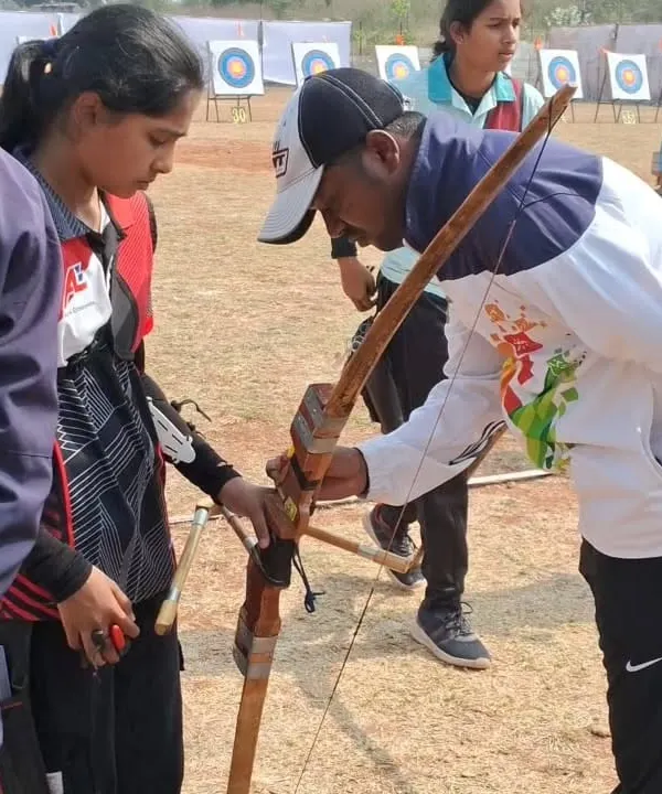 As a coach, my first priority is your safety and proper form. Here, I'm providing hands-on guidance to a student on how to correctly handle a traditional Indian bow, ensuring they build a strong foundation from their very first day.