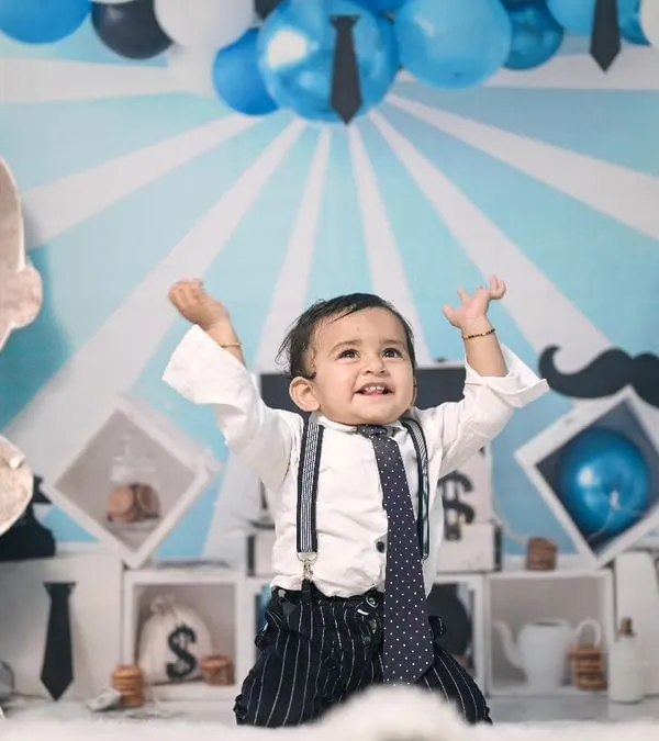 A perfect Boss Baby pose! This setup includes a custom-printed backdrop, a large character cutout, and themed props like money bags and a tie-motif balloon garland.