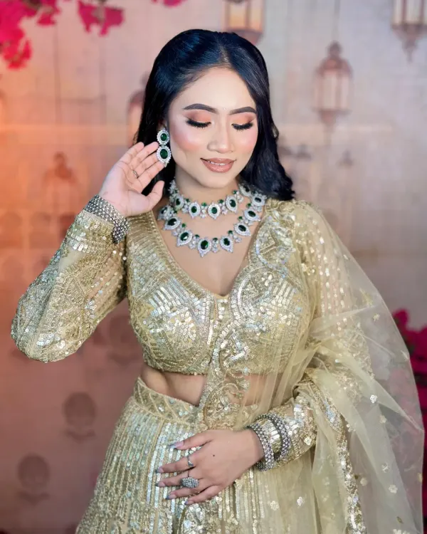 A beautiful soft glam look for an engagement ceremony. The focus is on flawless skin, gentle contouring, and shimmery eyes that complement the golden lehenga and emerald jewelry.