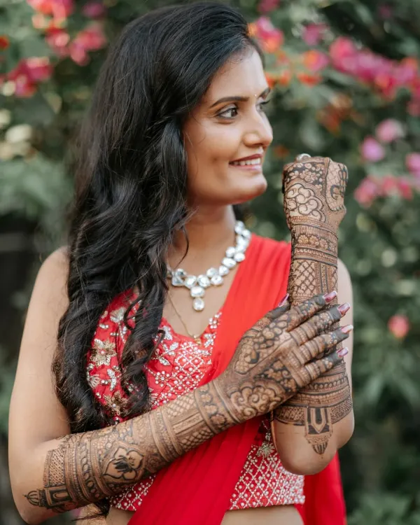 A radiant bride-to-be, her smile as bright as her red lehenga, showing off her intricate bridal mehendi.