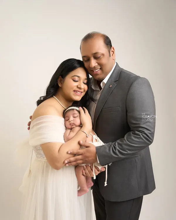 A classic family portrait in the studio. The parents embrace their sleeping newborn, creating a circle of love and protection. The simple white background keeps the focus entirely on their connection.