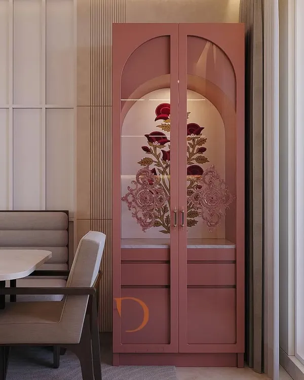 An elegant crockery unit in a soft pink finish, featuring arched glass doors with intricate floral artwork, perfectly integrated into a dining space.