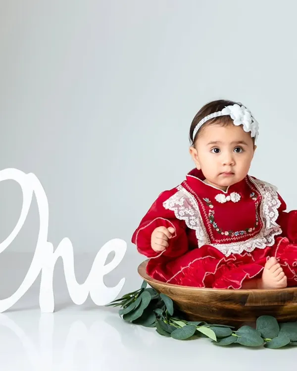 A simple and elegant portrait session featuring a beautiful red dress and a classic 'One' sign to mark the special milestone.
