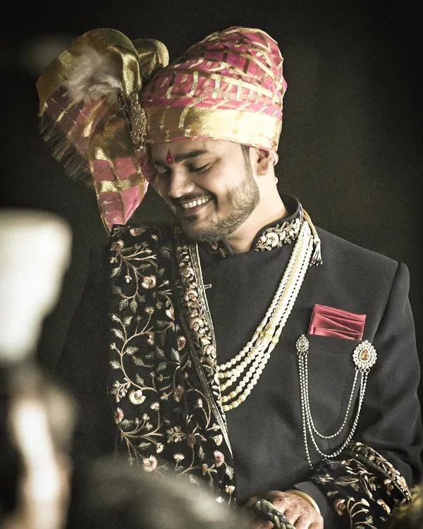 A candid portrait of the groom, capturing his happy and relaxed demeanor. His stylish sherwani, pearl necklace, and embroidered shawl showcase a perfect blend of traditional and modern groom fashion.