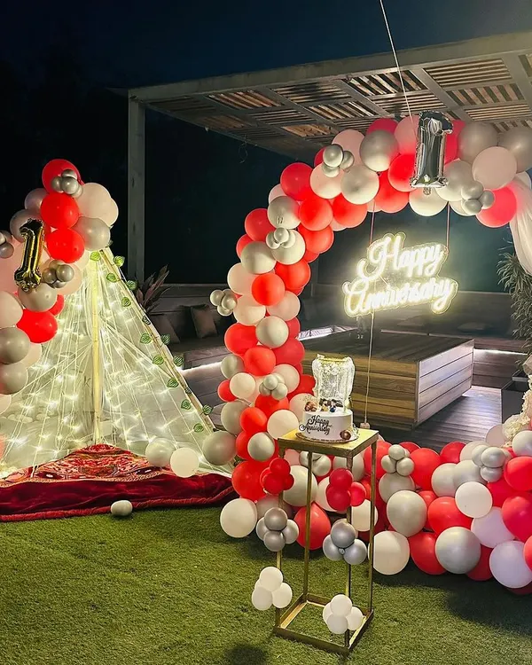 I designed this stunning outdoor setup for a first anniversary, featuring a full circular balloon arch in red, white, and silver. The custom "Happy Anniversary" neon sign and the lit-up cabana tent create a truly magical and memorable atmosphere for a terrace party.