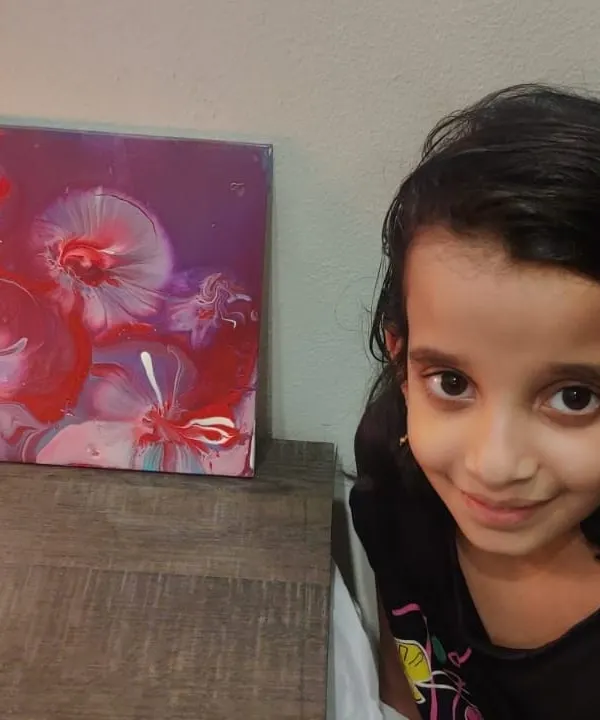 A young creator proudly posing next to her finished floral-like abstract painting. The patterns and colors in acrylic pouring are always a beautiful surprise.