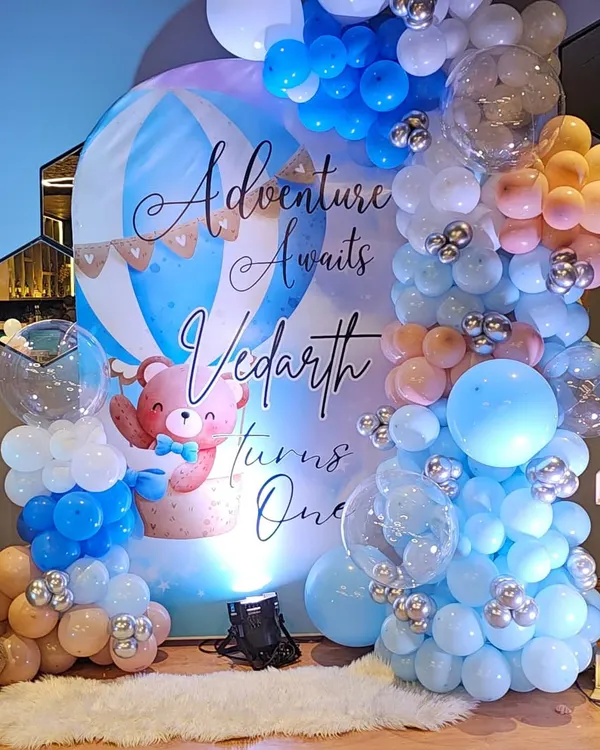 I believe every birthday is a grand adventure, especially the first one! This 'Adventure Awaits' theme with a hot air balloon backdrop, custom balloon garlands in soft blues and pastels, and a light-up number '1' creates a dreamy photo corner for Vedarth's special day.