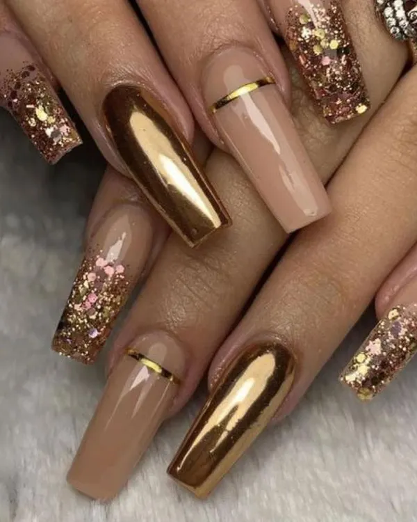 Make a bold statement with these dramatic coffin-shaped nail extensions. The design combines reflective gold chrome, nude polish, and sparkling gold glitter for a truly glamorous effect.