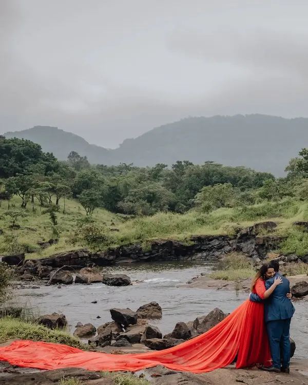 A dramatic pre-wedding portrait with the bride's flowing red dress against a stunning natural landscape. A moment of pure romance and artistry.
