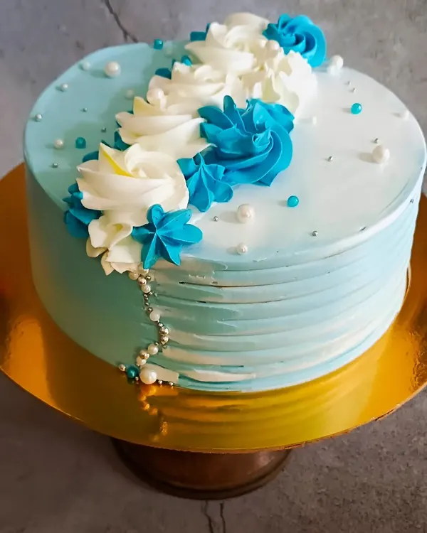 An elegant and simple cake design featuring a beautiful blue and white color palette. The buttercream is textured on the sides and decorated with piped rosettes and delicate sugar pearls.