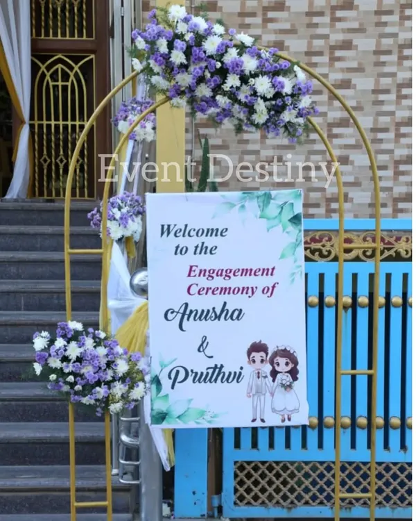 A charming welcome arch for an engagement ceremony. We used a simple golden arch decorated with purple and white floral bunches and a personalized welcome sign featuring a cute caricature of the couple.