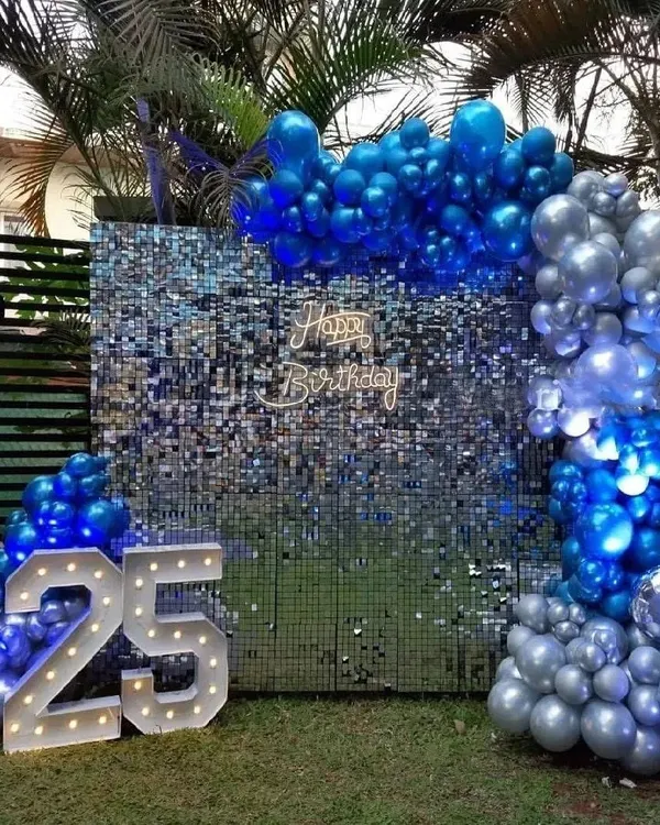 Celebrate a 25th birthday in style with this outdoor setup featuring large, illuminated marquee numbers. The blue and silver color scheme, paired with a blue shimmer wall, creates a cool and celebratory vibe perfect for a garden or lawn party.