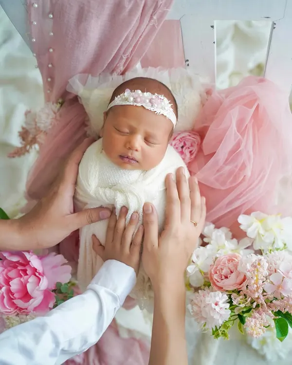 A dreamy portrait of a newborn nestled in a bed of soft pink florals and tulle. This artistic setup creates a magical, fairytale-like image of your sleeping baby.