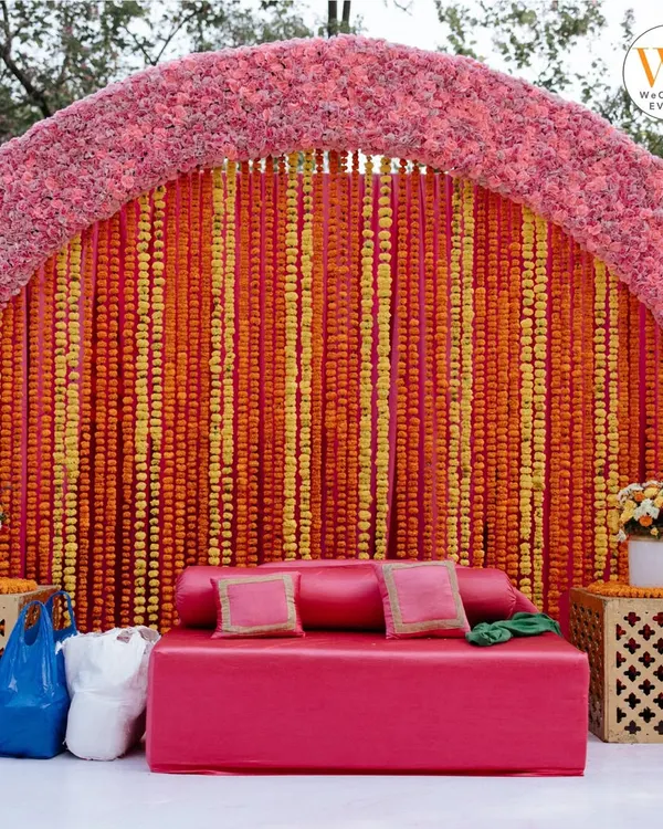 A classic Mehendi seating area is a must. I designed this one with a vibrant backdrop of orange and yellow marigold strings and a comfortable pink sofa for the bride.