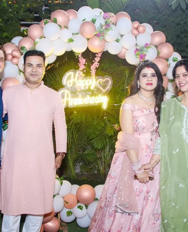 A couple celebrating with friends in front of a 'Happy Anniversary' neon sign at their outdoor party.