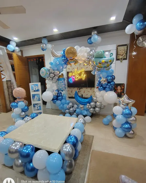 An elaborate welcome home decoration for a baby boy, filling the living room with joy. This setup features a large balloon arch with a "Welcome Baby" neon sign, "BABY" blocks, and balloons surrounding a central table.