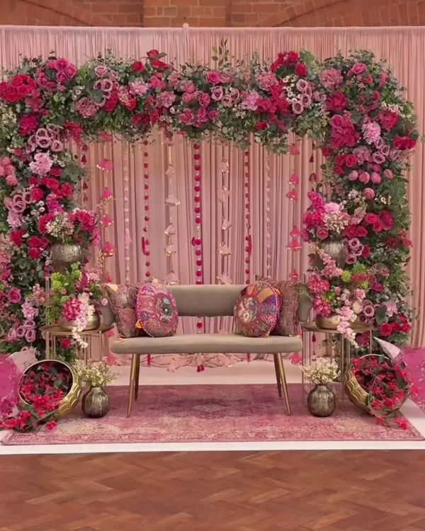 A luxurious Mehendi or engagement stage completely decorated in shades of pink. The setup features a massive floral arch, a backdrop of pink drapes, and elegant seating, creating a romantic and opulent look.