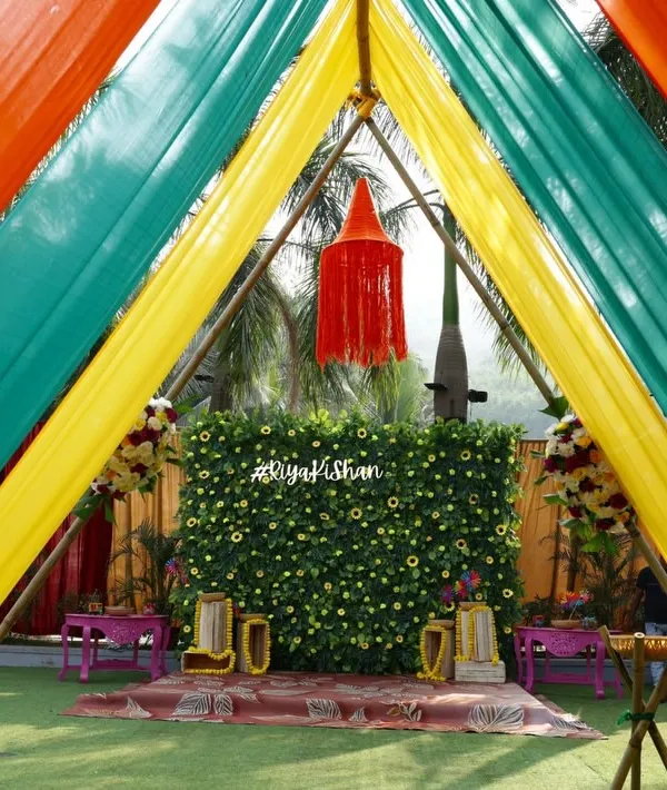 A close-up of our colorful Haldi entrance tunnel. The combination of yellow, green, and orange drapes frames the beautiful floral backdrop, creating a perfect photo opportunity for guests as they arrive.