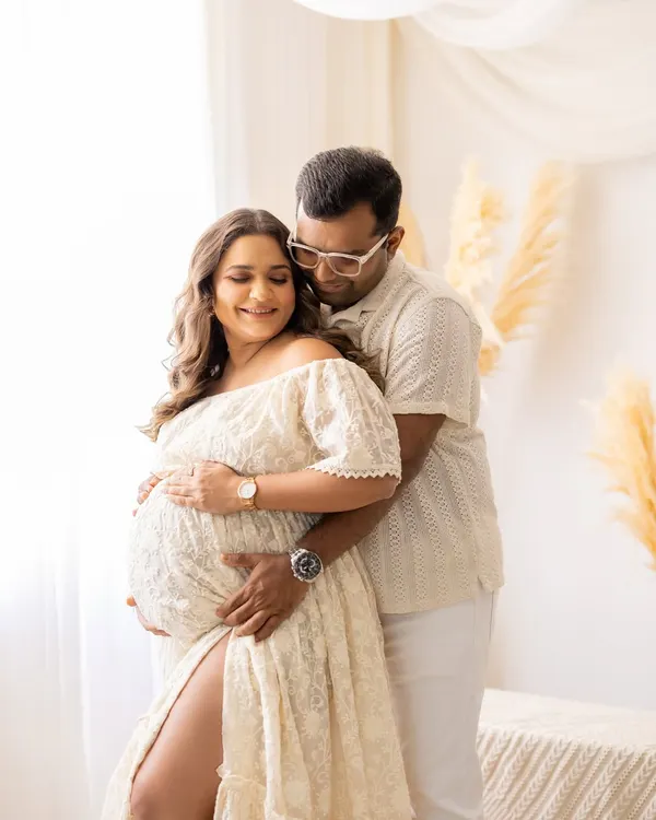 This couple is bathed in soft window light in my studio. The mother-to-be, wearing a beautiful off-white lace gown, cradles her bump while her partner embraces her from behind, creating a tender and romantic maternity portrait.
