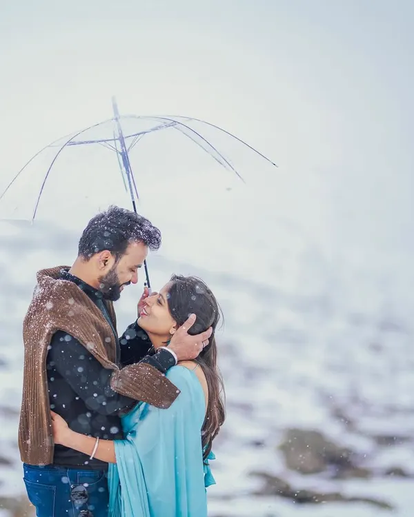A classic romantic movie moment recreated in the snows of Gulmarg. The couple huddles close under a clear umbrella as snowflakes fall around them, creating a magical and intimate pre-wedding portrait.
