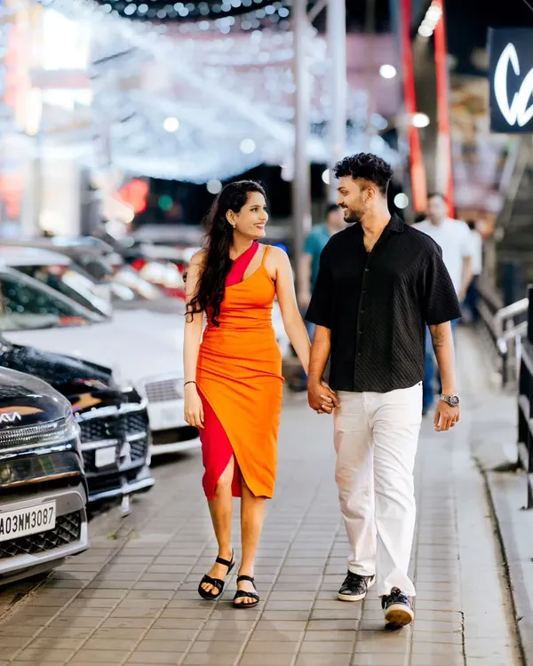 A full-length shot of a couple walking hand-in-hand down a city street at night, with decorative lights creating a beautiful bokeh background.