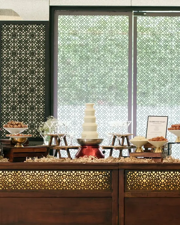 An elaborate dessert buffet featuring a white chocolate fountain and an array of Indian sweets. Our buffet setups are designed to be a visual spectacle, inviting guests to indulge in a thoughtfully curated selection of treats.