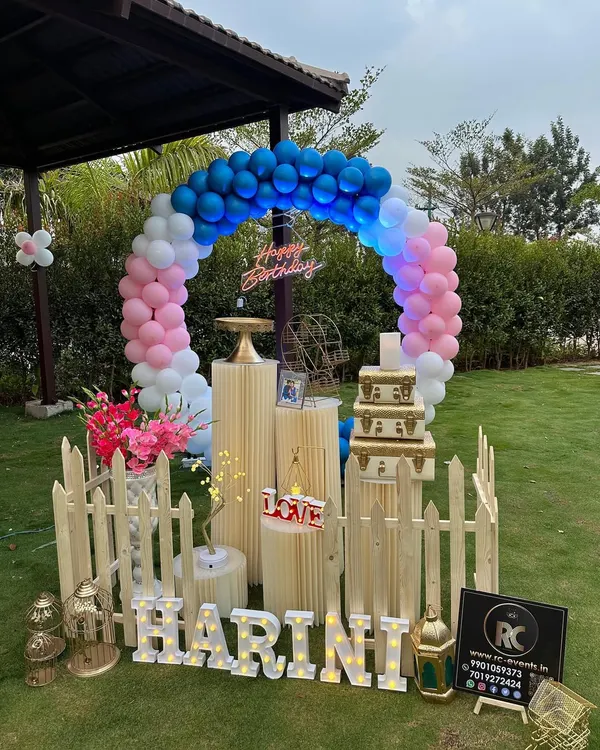 Our decorations are perfect for outdoor settings too. Here, we set up a colorful balloon arch and a personalized display with the name 'HARINI' in marquee letters for a beautiful garden party. The picket fence and props add a charming, rustic feel.