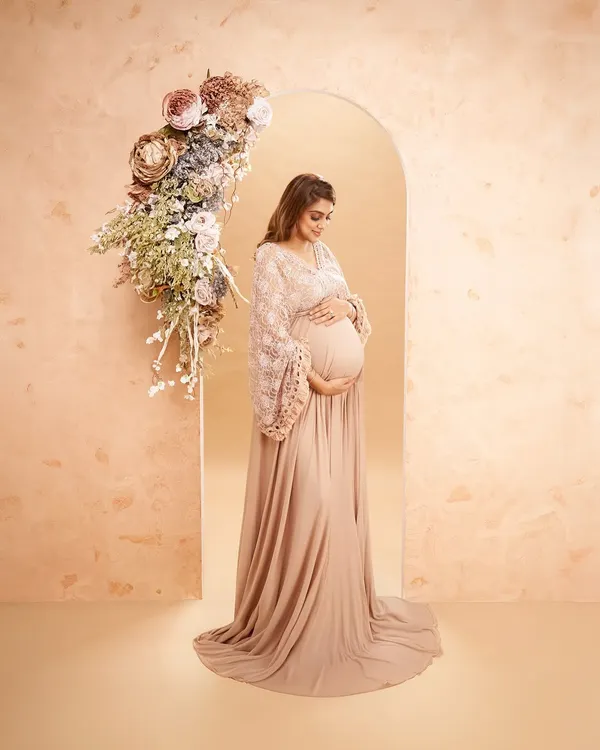 A beautiful portrait featuring a custom-built floral arch. The warm, peach-toned backdrop and elegant gown come together to create a sophisticated and artistic floral-themed shot.