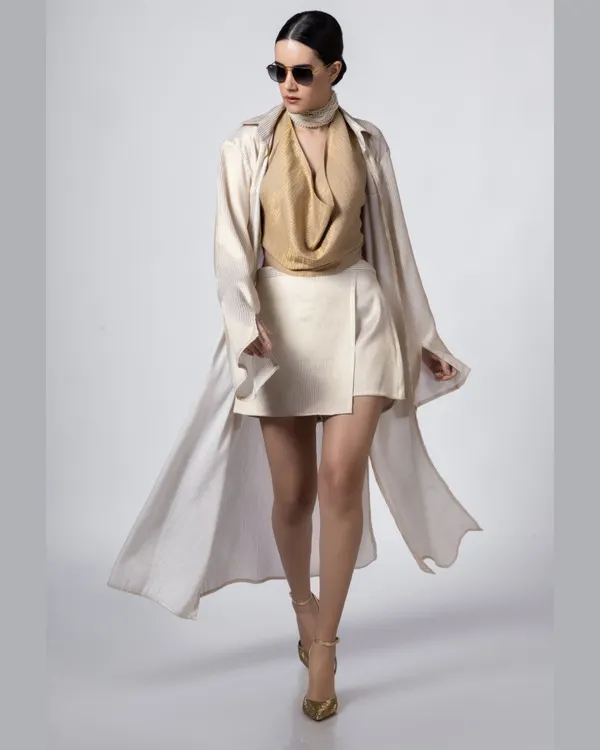 A full-length shot of a model in a flowing beige trench coat and white skirt, walking with confidence. This image captures a sense of movement and high fashion, perfect for an editorial spread or a designer lookbook.