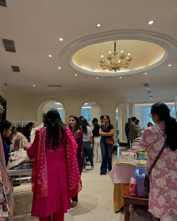 A wide view of the exhibition hall, showing a steady stream of visitors browsing different stalls under the elegant chandeliers of the clubhouse.
