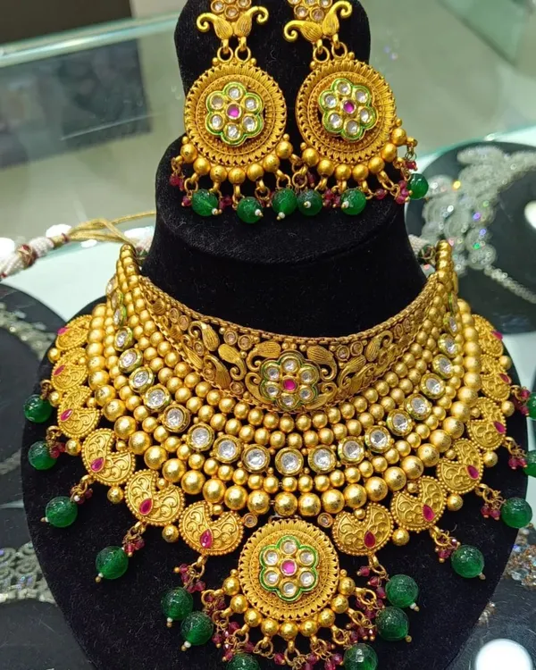 This bridal necklace set has a beautiful antique gold finish with detailed meenakari work in green and pink. The matching earrings with green bead drops complete this traditional look, making it feel like authentic gold jewellery.