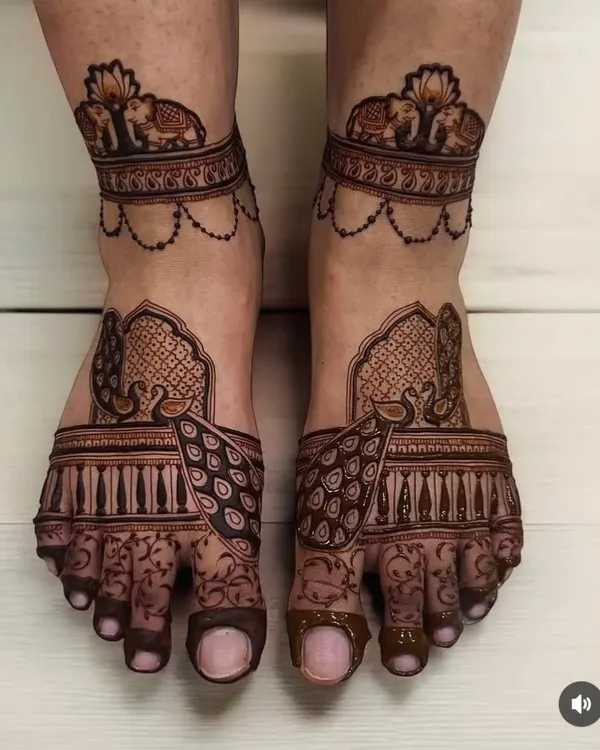 A perfect example of regal foot mehndi. This symmetrical design features majestic peacocks on the top of the feet and a band of elephants around the ankles.