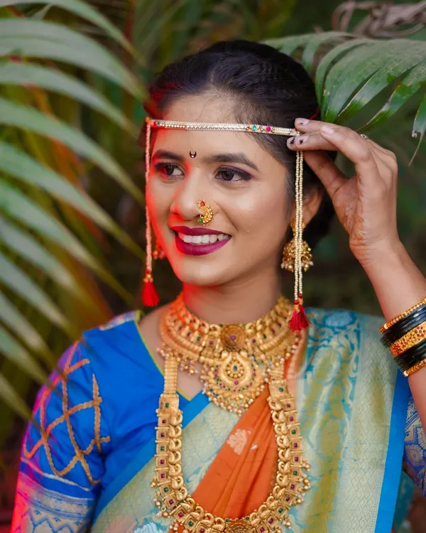 A close-up of a stunning Maharashtrian bride. The focus is on her radiant smile and the traditional details like the 'bashing' and heavy gold jewelry, complemented by soft, flattering light.