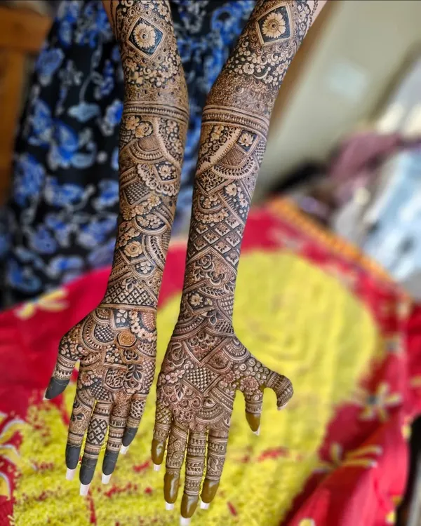 A stunning Dubai-style bridal mehendi that extends to the elbows. The design features a mix of bold floral patterns, intricate netting, and paisley elements.