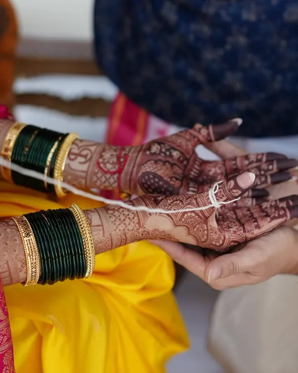 The beauty of a rich henna stain during a wedding ceremony. The deep maroon color of the mehendi contrasts beautifully with the bride's yellow saree and green bangles.