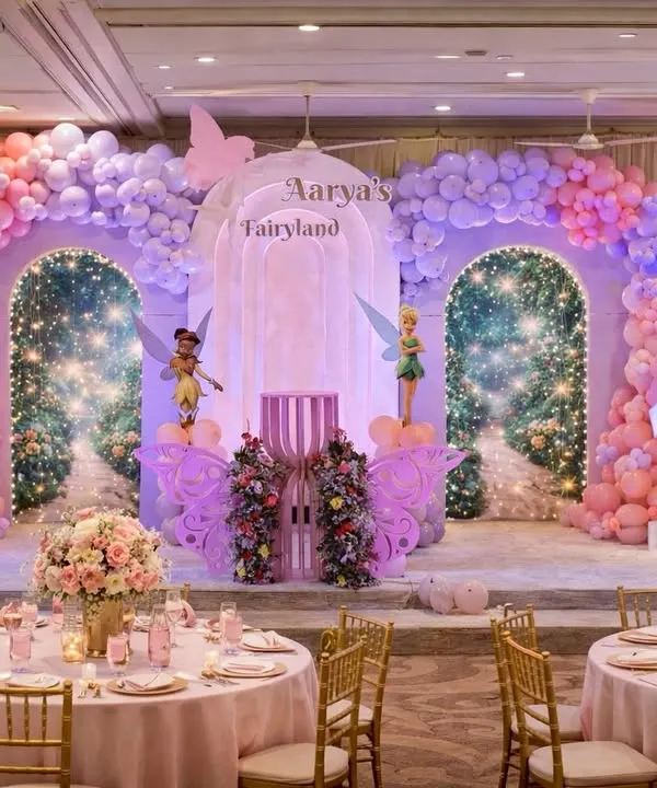 A complete "Fairyland" setup for Aarya's first birthday. This magical stage features Tinkerbell, large butterfly wings, sparkling archways, and coordinated floral table arrangements for a fully immersive experience.
